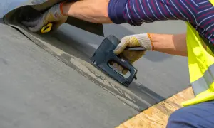 Ręce w rękawicach mocują papę na dachu za pomocą zszywacza.