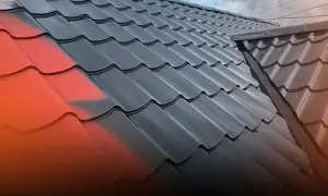 Fragment dachu z blachy, częściowo pomalowany na czerwono, częściowo na czarno.