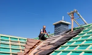 Cieśla kładzie dachówki na budowie dachu pod błękitnym niebem.