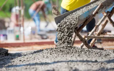 Beton wylewany z rynny na placu budowy. Warto wiedzieć, ile waży kubik betonu, by zaplanować prace.