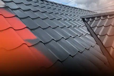 Fragment dachu z blachy, częściowo pomalowany na czerwono, częściowo na czarno.