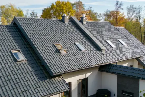 Nowoczesna blacha na dach pokrywa dom z kilkoma oknami dachowymi. Jesienne drzewa otaczają budynek.